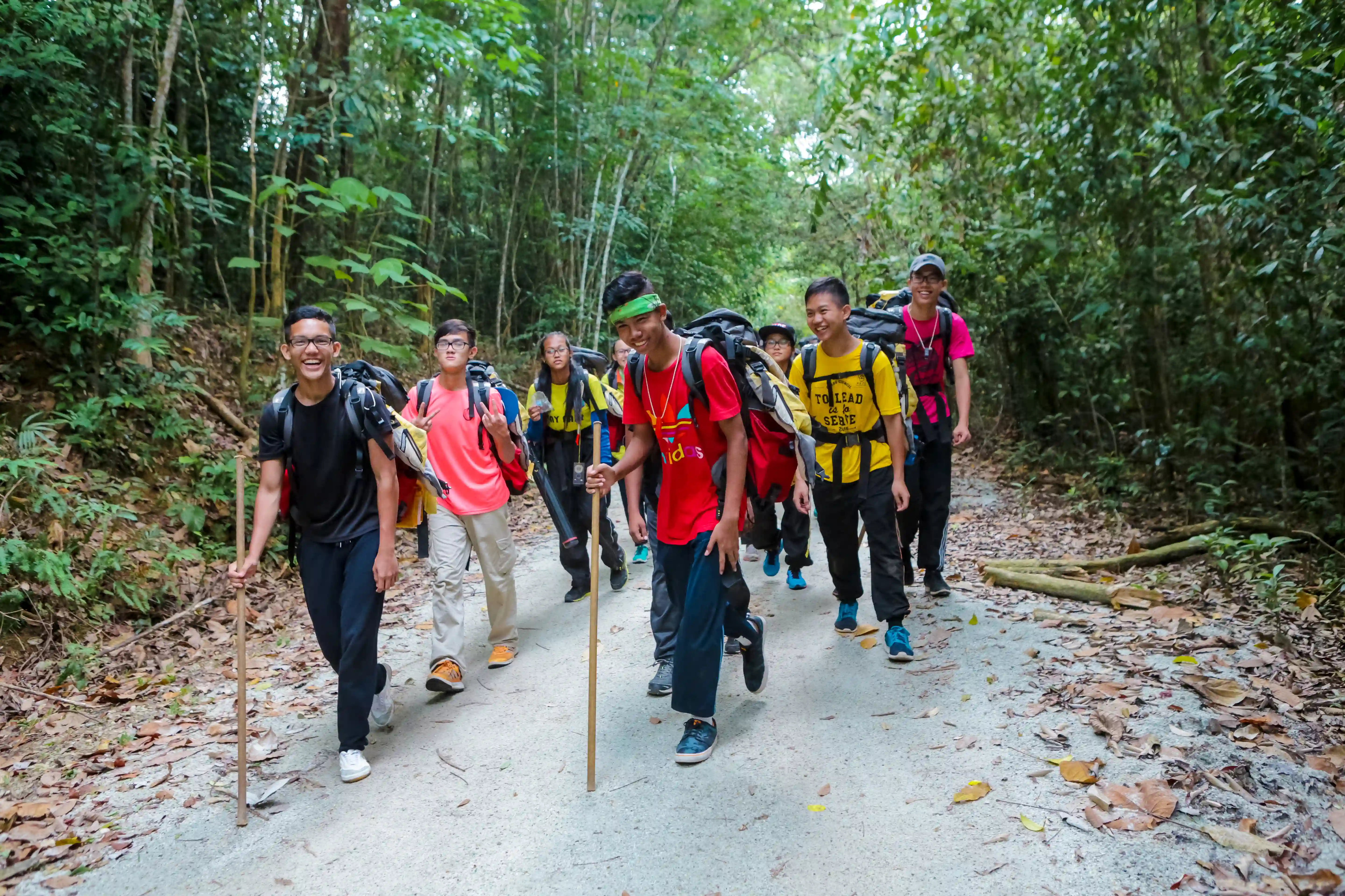 Youths trek with backpacks and walking sticks through a forest trail during an expedition.